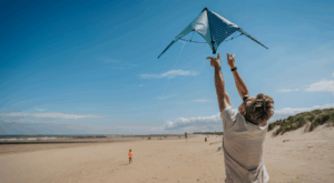 ein Mann mit Sonnenbrille lässt an einem Strand einen Drachen steigen.